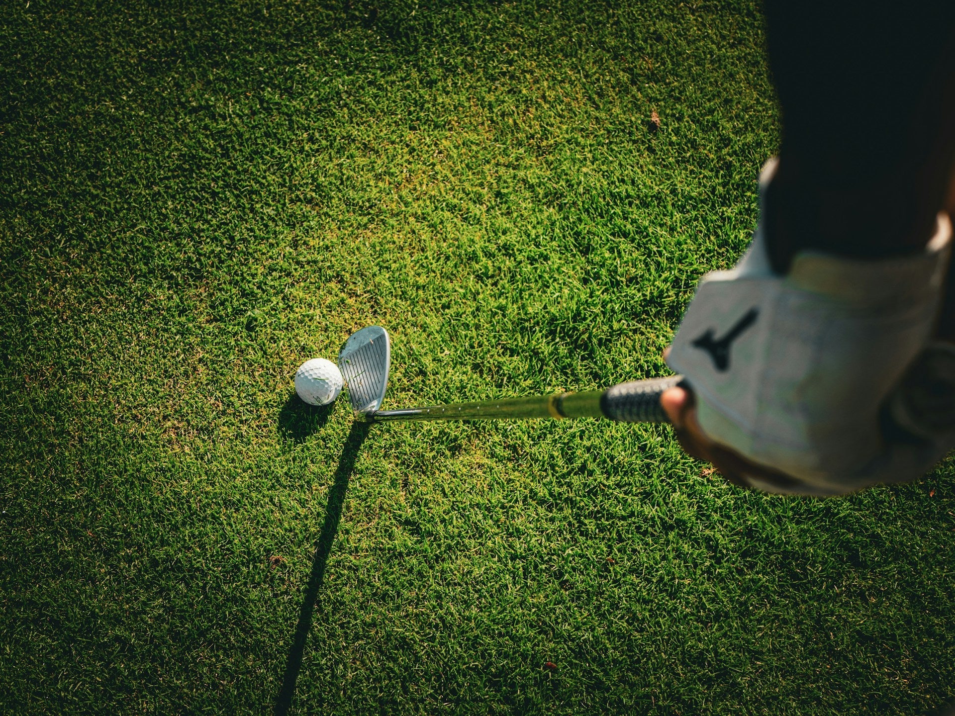 detail of a golf player holding a iron golf club about to hit a golf ball