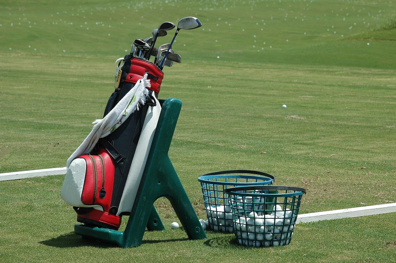 golf bag standing in a golf field with clubs inside, next to baskets with golf balls