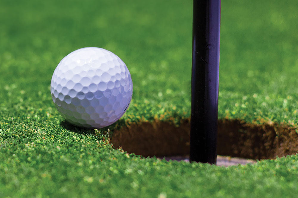 golf ball next to golf hole close view