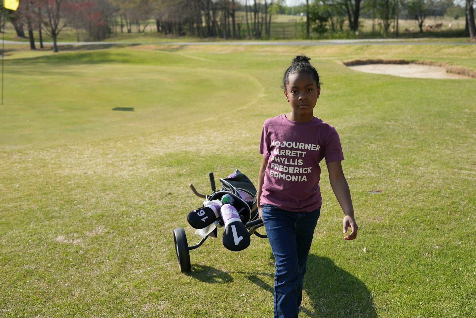 Kid walking in a green golf field with a complete set of children's golf clubs