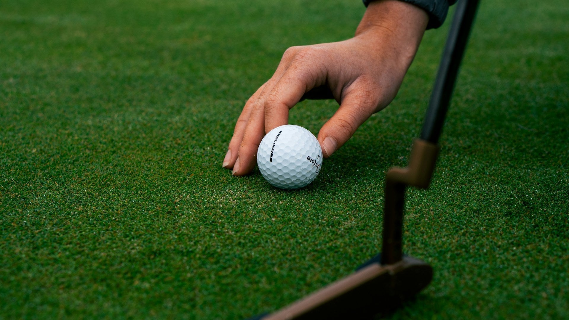 golf player setting a golf ball close to a putter before putting