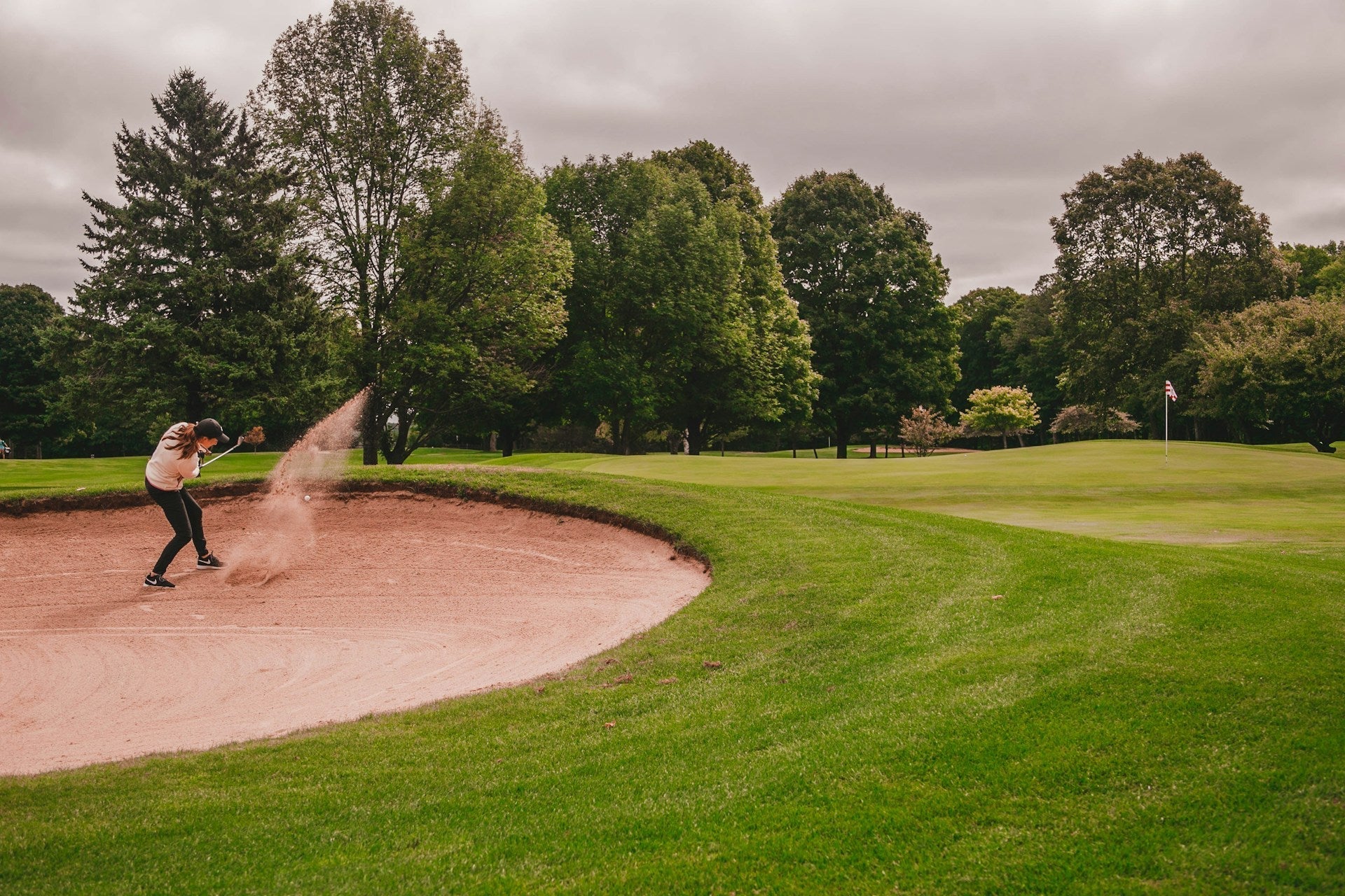 Woman player hitting a ball in the sand with a golf club for women