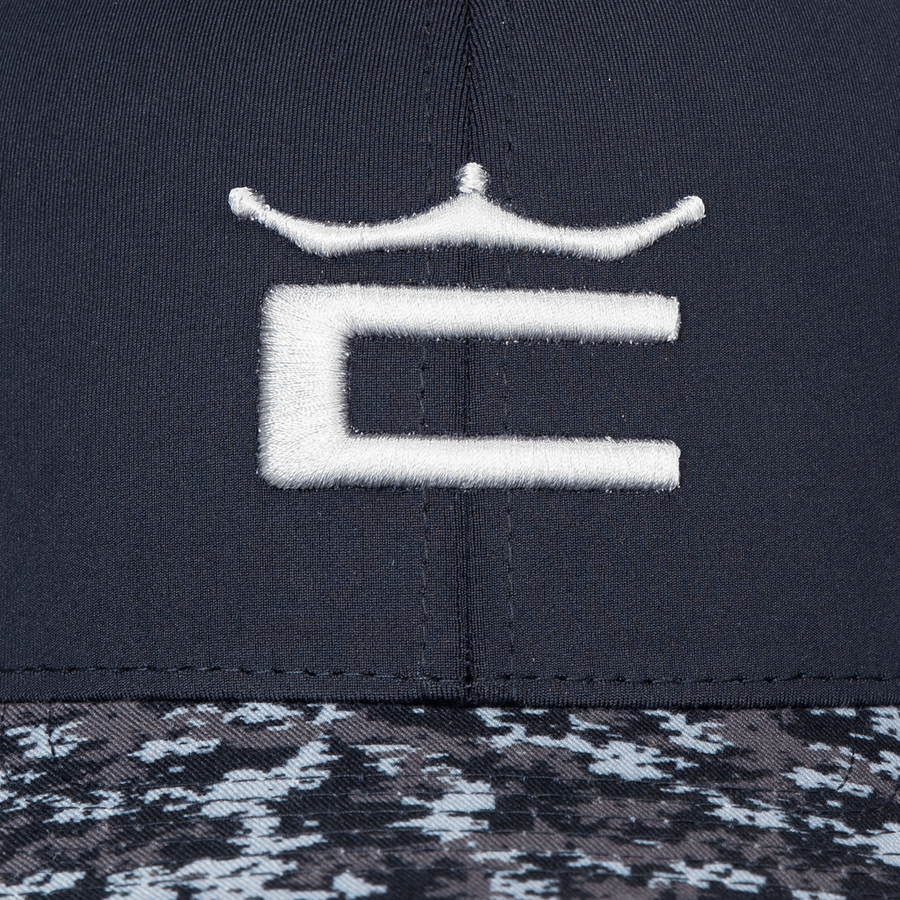 A close-up of the Cobra Camo Crown C Snapback Cap shows a white embroidered C with a crown, a black/gray/white digi-camo color block brim, and comfortable Flexfit 110 sweatband.