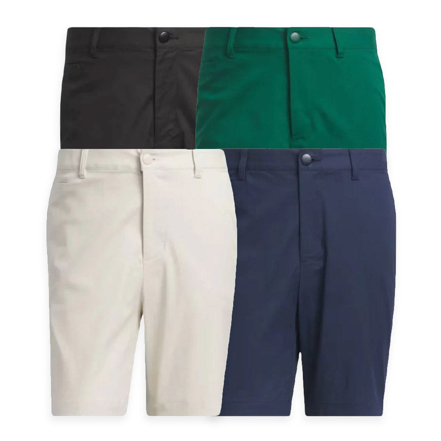 Four pairs of Adidas Go-To Five-Pocket Golf Shorts in black, green, white, and navy blue are displayed front-facing side by side, each featuring belt loops and a button closure.