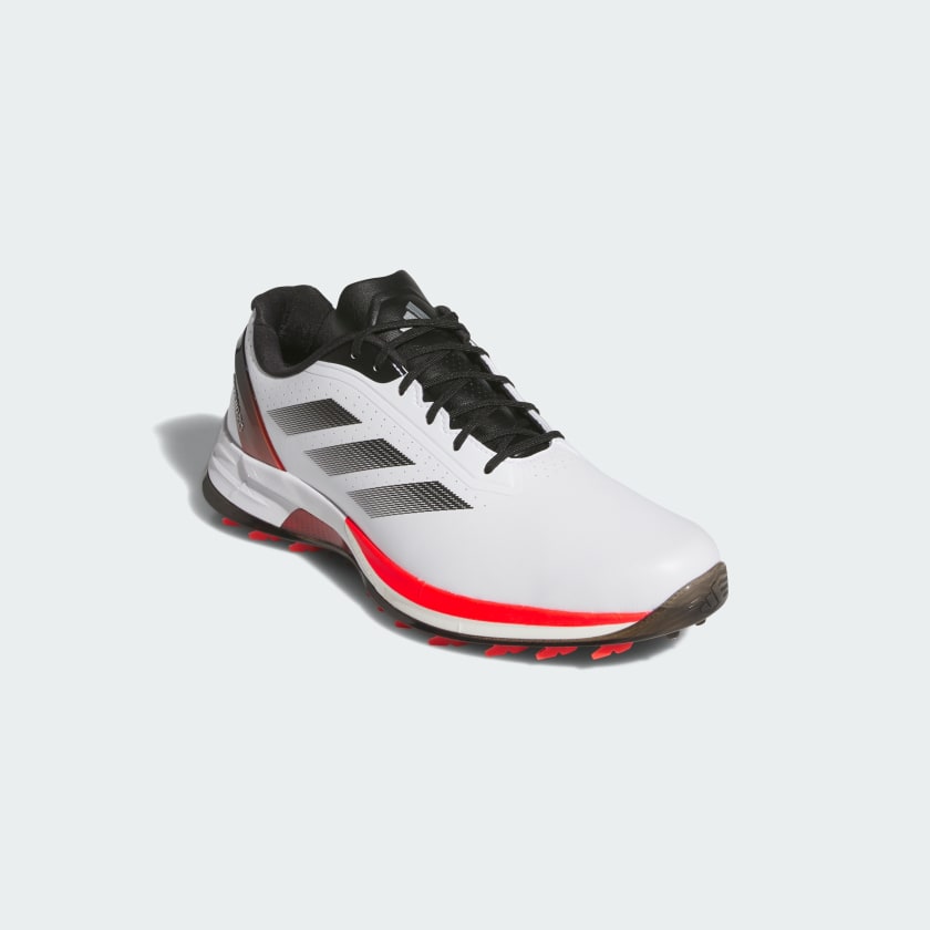 The Adidas Adizero ZG Spikeless Golf Shoes in White/Red feature a waterproof upper, black laces, black tongue, three black side stripes, and red midsole accents, shown on a light gray background.