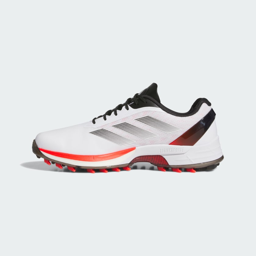 The Adidas Adizero ZG Spikeless Golf Shoes in White/Red feature a waterproof white upper, black and red accents, a black sole with red treads, and side mesh panels for breathability.