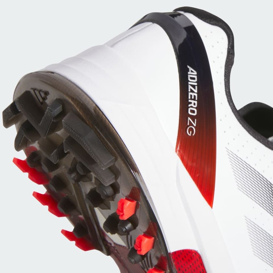 Close-up of the Adidas Adizero ZG Spikeless Golf Shoes in white/red, showing the black and red studded sole, waterproof upper, and ADIZERO ZG printed on the side.