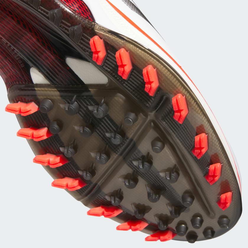 Close-up of the sole of Adidas Adizero ZG Spikeless Golf Shoes in White/Red, featuring a transparent section with red and black rubber spikes for traction—crafted using recycled materials for eco-friendly performance.
