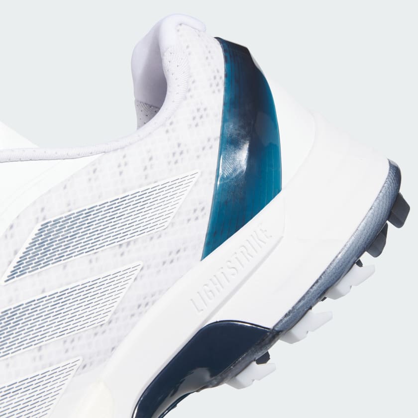 Close-up of the heel and side of the Adidas Adizero ZG Spikeless Golf Shoes in white/blue, featuring a textured pattern, blue accents, and LIGHTSTRIKE midsole. Made with recycled and renewable materials for grip and sustainability.