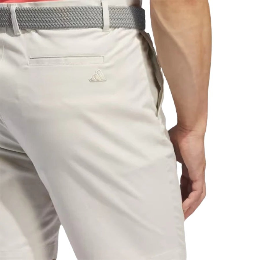 A person seen from the back wearing Adidas Go-To Five-Pocket Golf Shorts in light beige with a gray braided belt. The shorts have a back pocket and a small Adidas logo above it.