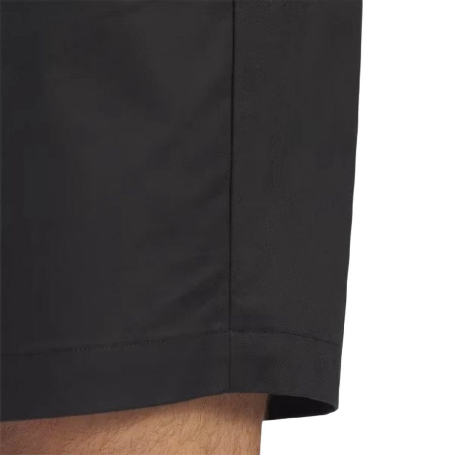 Close-up of the lower portion of a person wearing Adidas Go-To Five-Pocket Golf Shorts in black, showcasing the hemline and part of a bare leg against a plain background.