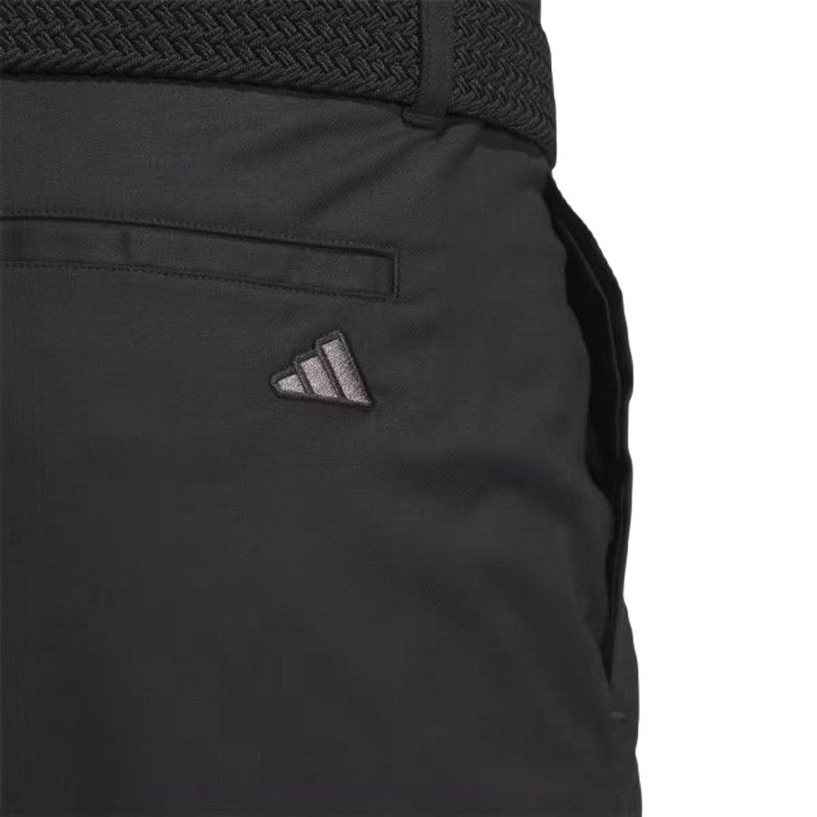 Close-up of Adidas Go-To Five-Pocket Golf Shorts in black, featuring a small embroidered adidas logo near the back pocket and a braided black belt at the waistband.