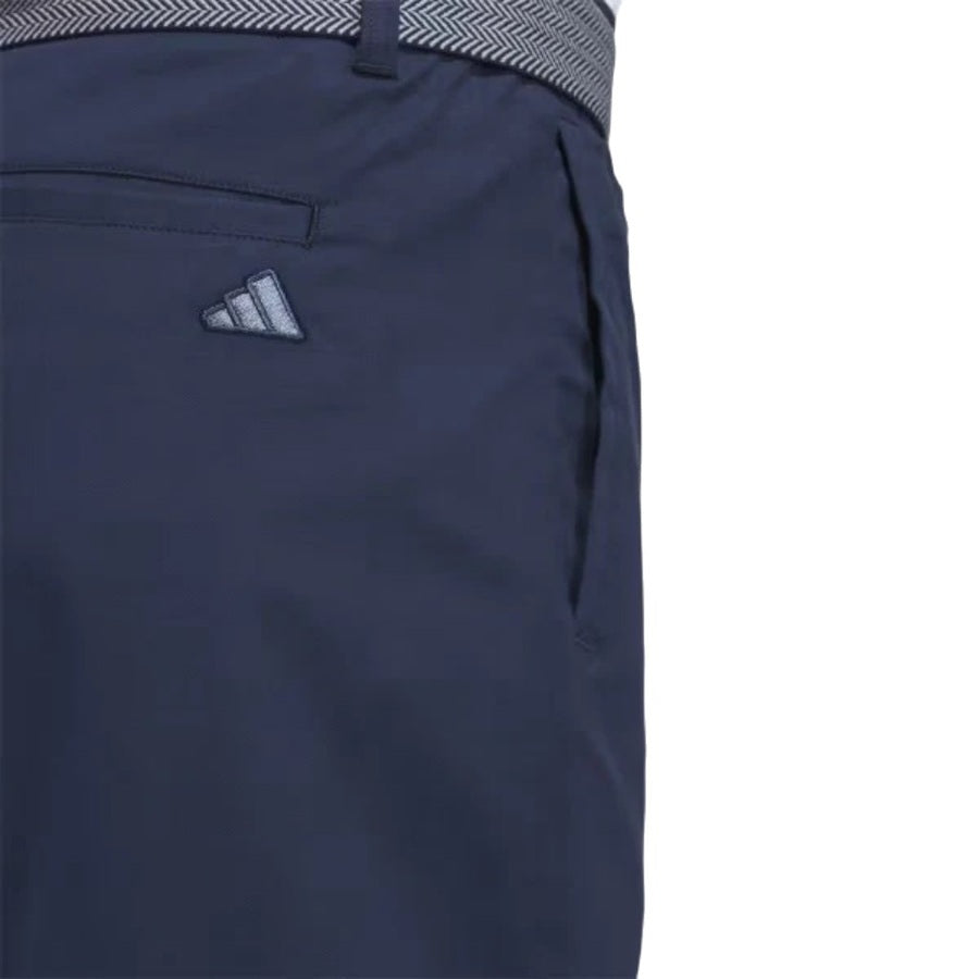 The image features the Adidas Go-To Five-Pocket Golf Shorts in navy blue, showcasing a visible back pocket, patterned waistband, and iconic logo against a crisp white background.