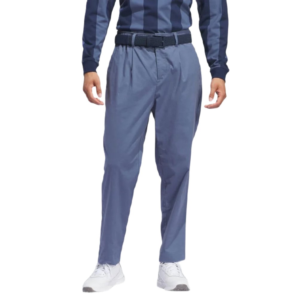 A person wears Adidas Go-To Versatile Pants - Blue made from recycled materials, paired with a blue striped long-sleeve shirt, blue belt, and white sneakers. The image is cropped from the shoulders down with arms relaxed at their sides.