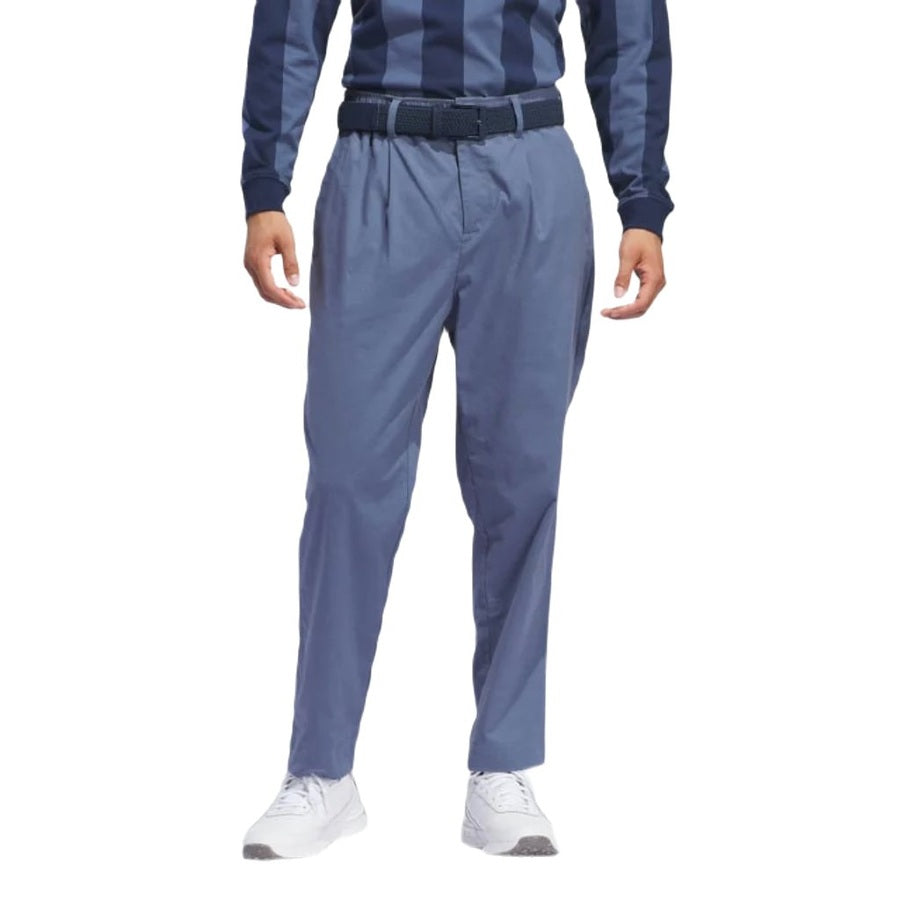 Une personne porte un pantalon Adidas Go-To Versatile bleu en matières recyclées, associé à une chemise bleue à rayures à manches longues, une ceinture bleue et des baskets blanches. L’image est recadrée des épaules vers le bas, bras le long du corps.