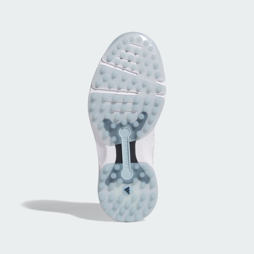 The image shows the bottom of the Adidas MC Zoysia Ladies Spikeless Golf Shoes in white, featuring a translucent textured sole with circular grip patterns, BOOST cushioning, and a central TORSION SYSTEM support bar.