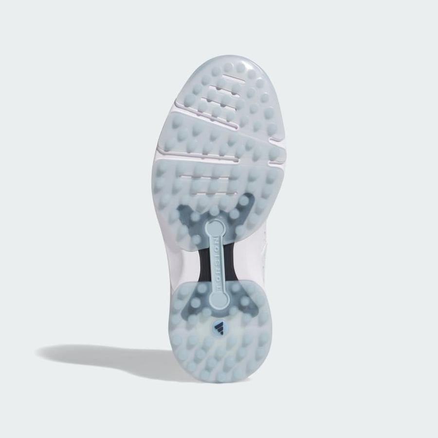 The image shows the bottom of the Adidas MC Zoysia Ladies Spikeless Golf Shoes in white, featuring a translucent textured sole with circular grip patterns, BOOST cushioning, and a central TORSION SYSTEM support bar.