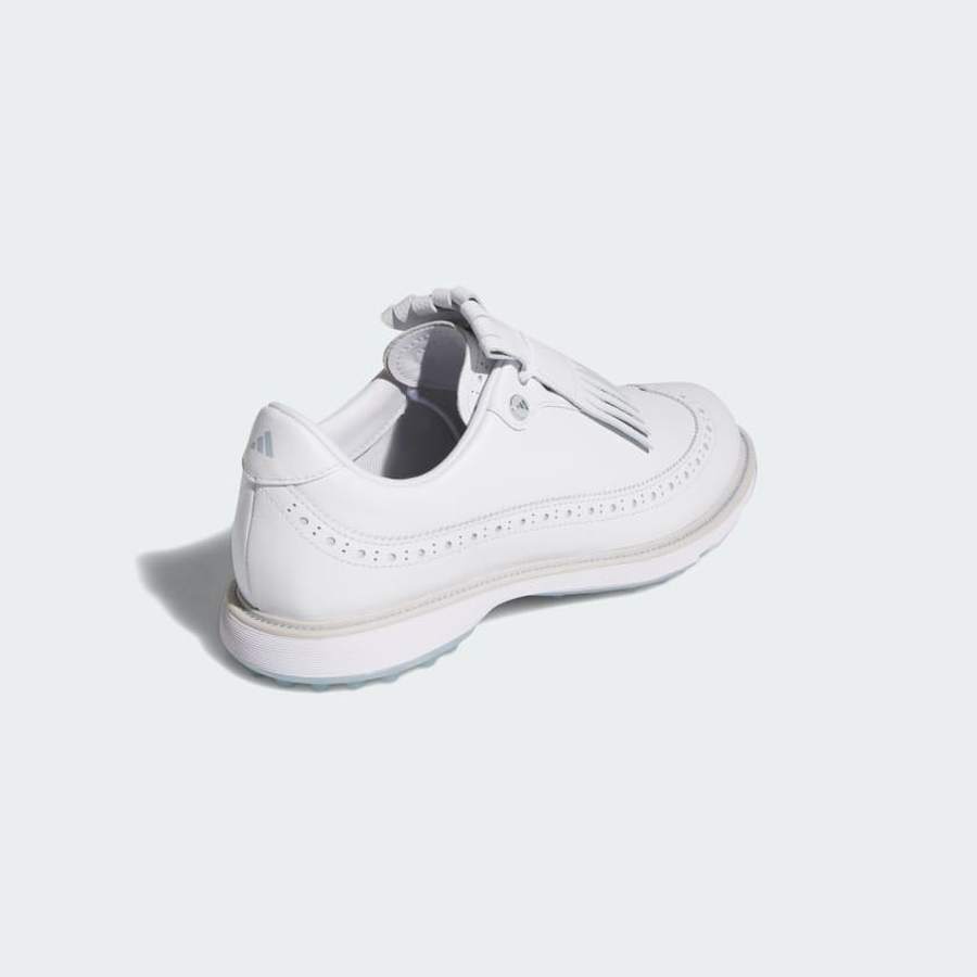 The Adidas MC Zoysia Ladies Spikeless Golf Shoes in white, shown from a rear angle on a light background, feature decorative perforations, a textured Torsion System sole, and fringe detail covering the laces.