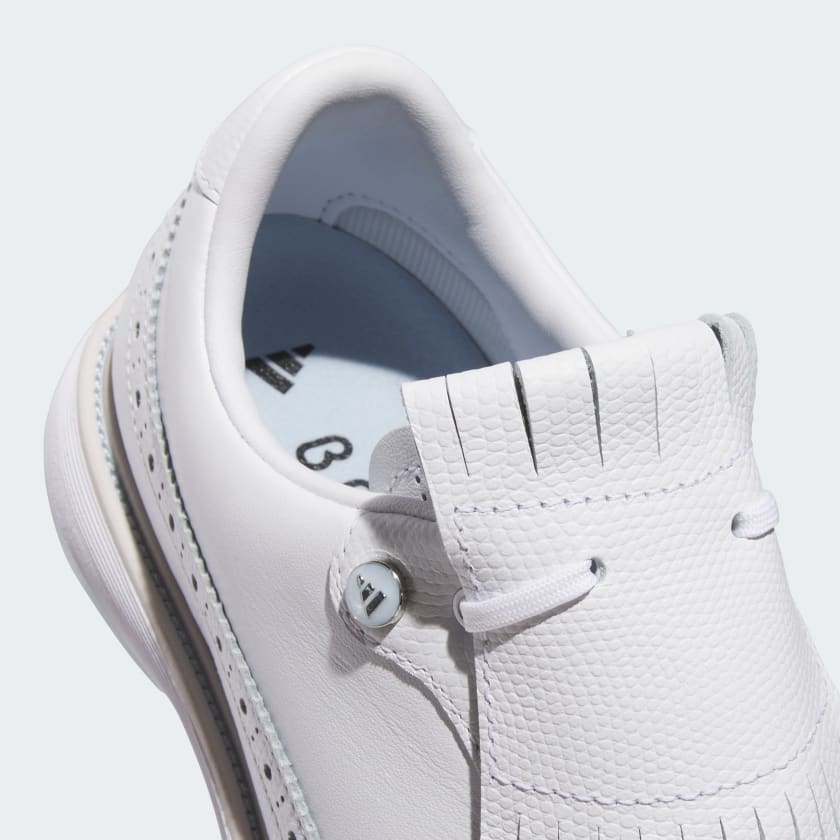 Close-up view of the Adidas MC Zoysia Ladies Spikeless Golf Shoes in white, featuring textured leather, decorative stitching, fringe on the tongue, white laces, visible interior with printed branding, and advanced BOOST cushioning.