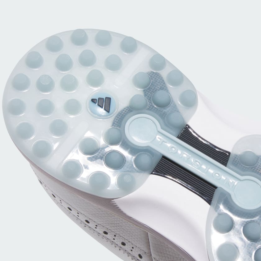 Close-up of the sole of the Adidas MC Zoysia Ladies Spikeless Golf Shoes - White, showing translucent spikes, textured grip patterns, BOOST branding, and “TORSION” on the Torsion System midfoot support bar.