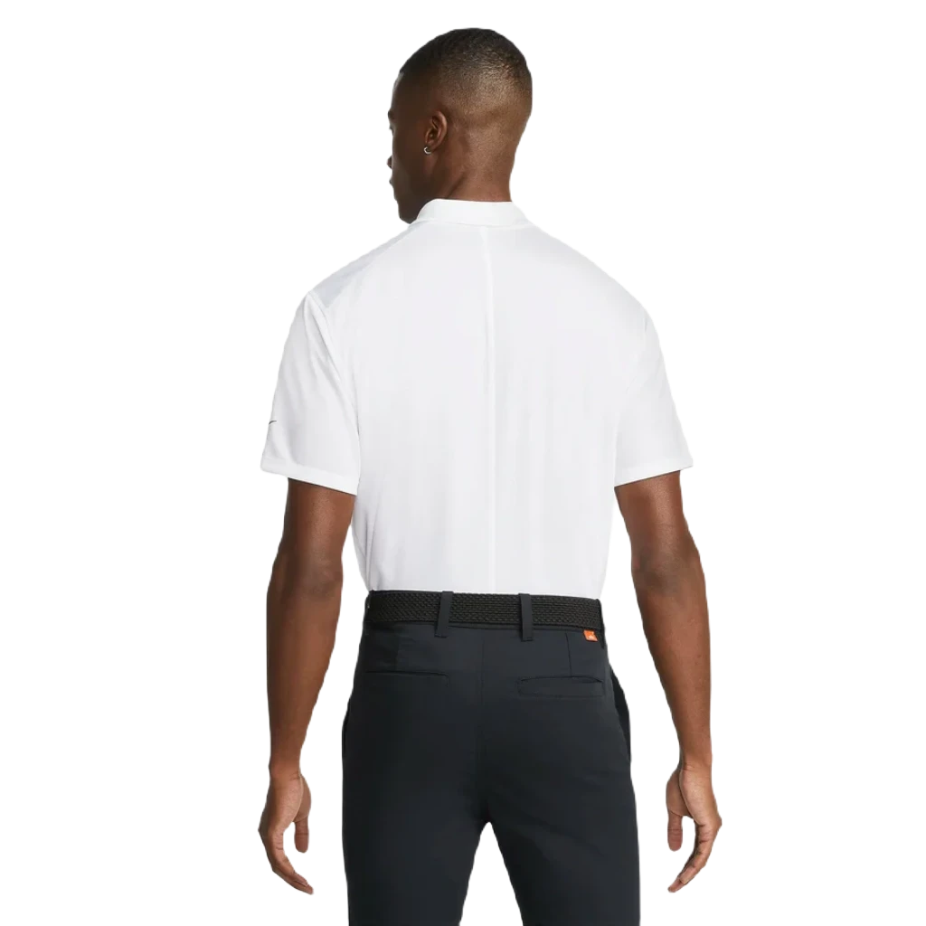 A man faces away, wearing a white Nike Dri-FIT Victory Men's Golf Shirt with a course/event logo, tucked into dark pants and paired with a black woven belt, set against a plain white background.