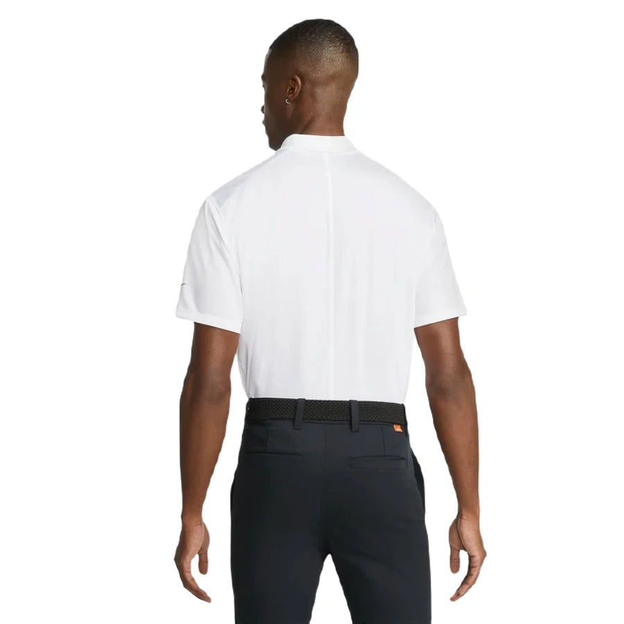 A man faces away, wearing a white Nike Dri-FIT Victory Men's Golf Shirt with a course/event logo, tucked into dark pants and paired with a black woven belt, set against a plain white background.