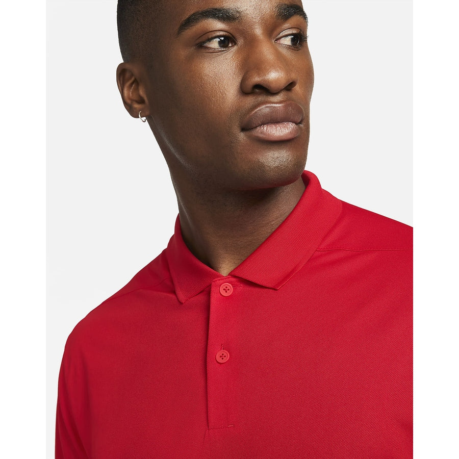 A man in a vibrant red Nike Dri-FIT Victory Men's Golf Shirt with a course/event logo stands against a plain white background, gazing off to the side with a neutral expression.