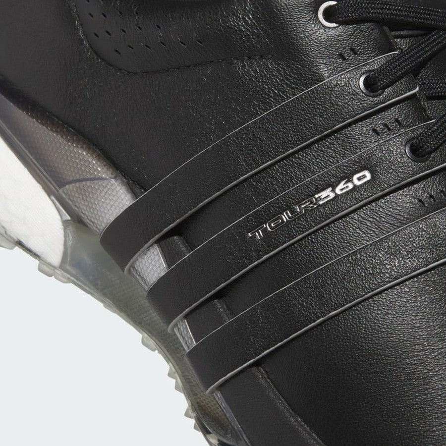 Close-up of Adidas Tour360 25 Spikeless Golf Shoes in black, showcasing three diagonal stripes, silver TOUR360 branding, perforated leather, and a partially visible transparent outsole with BOOST and 3D Traxion technology.