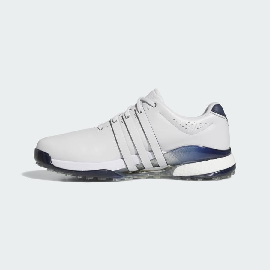 The Adidas Tour360 25 Spikeless Golf Shoes in grey feature navy accents, three side stripes, a lace-up closure, and a 3D Traxion outsole for grip. Displayed in side profile against a light background.