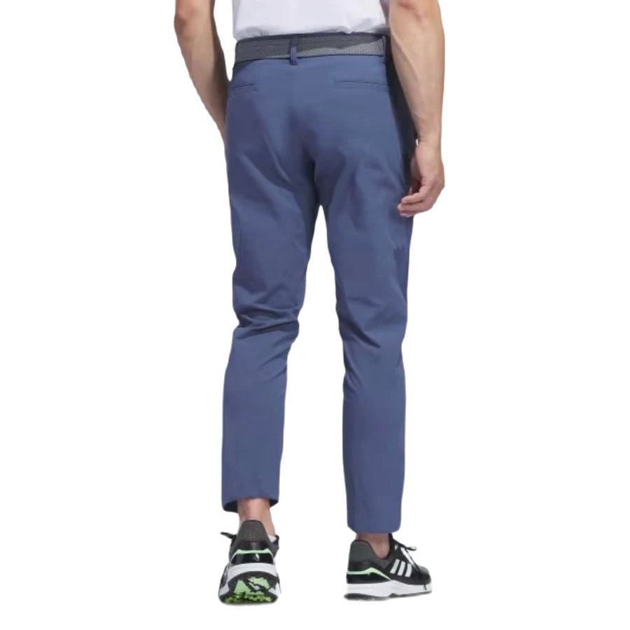 A person wearing blue Adidas Ultimate365 Chino Pants, made with recycled materials, a gray belt, and black athletic shoes with white soles, shown from the back on a white background.