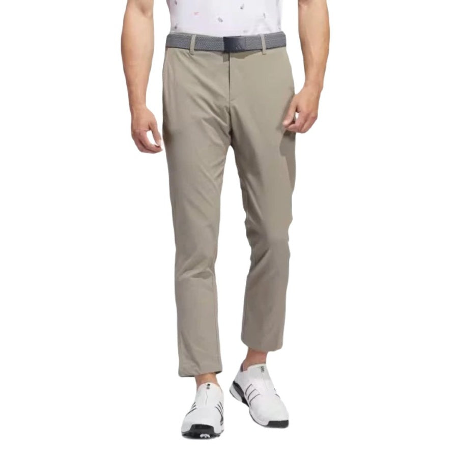A man wearing light khaki Adidas Ultimate365 Chino Pants made from recycled materials, a gray belt, white sneakers, and a white patterned polo. The image is cropped from shoulders down.