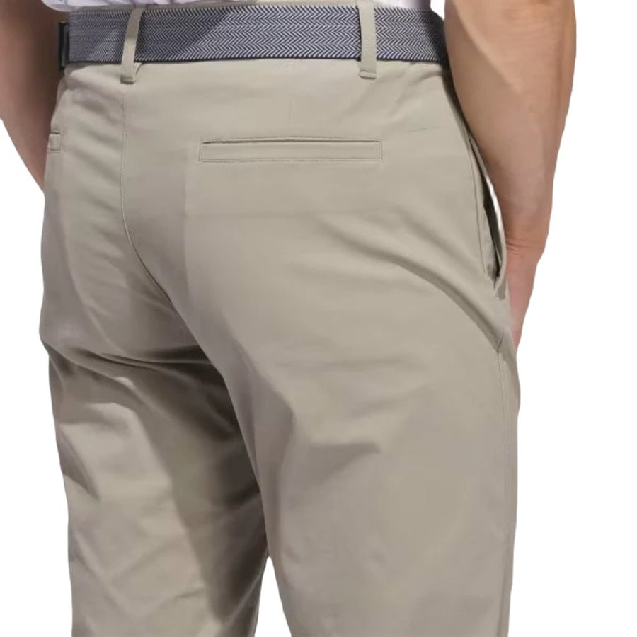 A person wearing light beige Adidas Ultimate365 Chino Pants with a patterned belt, viewed from the back at waist level. Made with recycled materials, these pants have two rear welt pockets.