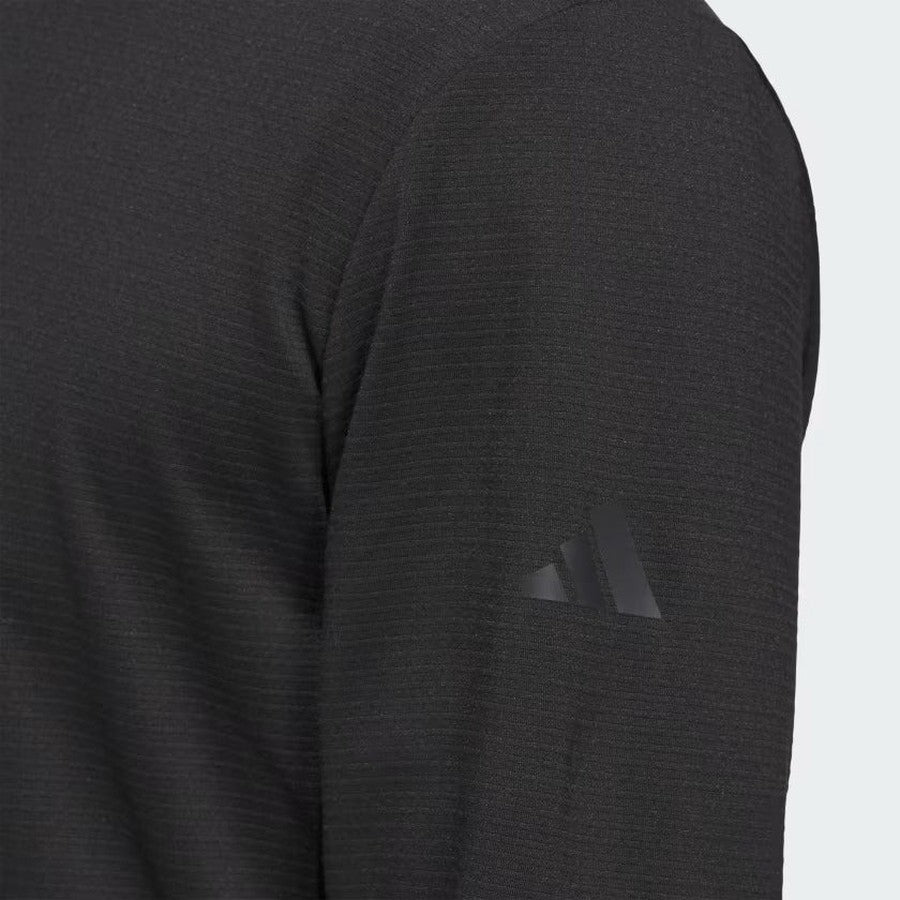 Close-up of a person in the Adidas Ultimate365 Elevated Pullover Hoodie, a long-sleeved, dark-colored golf top with a subtle upper arm logo. Made from recycled materials, it stands out against a plain, light background.