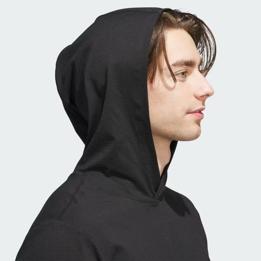 A young person with light skin and brown hair wears the Adidas Ultimate365 Elevated Pullover Hoodie, made from recycled materials, with the hood up, shown in profile against a light gray background.