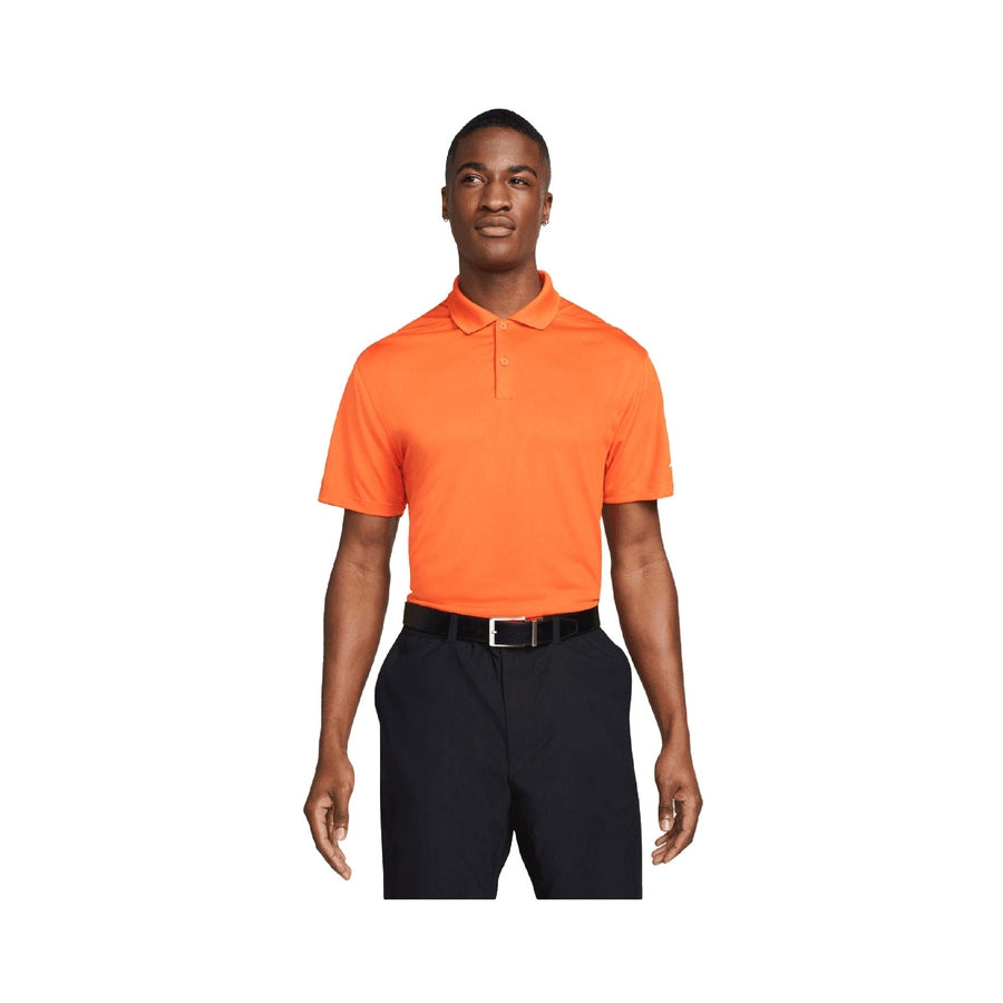 A man faces forward, wearing a Nike Dri-FIT Victory Men's Golf Shirt - Course/Event Logo - Final Sale in orange, tucked into black pants with a black belt, set against a plain white background.