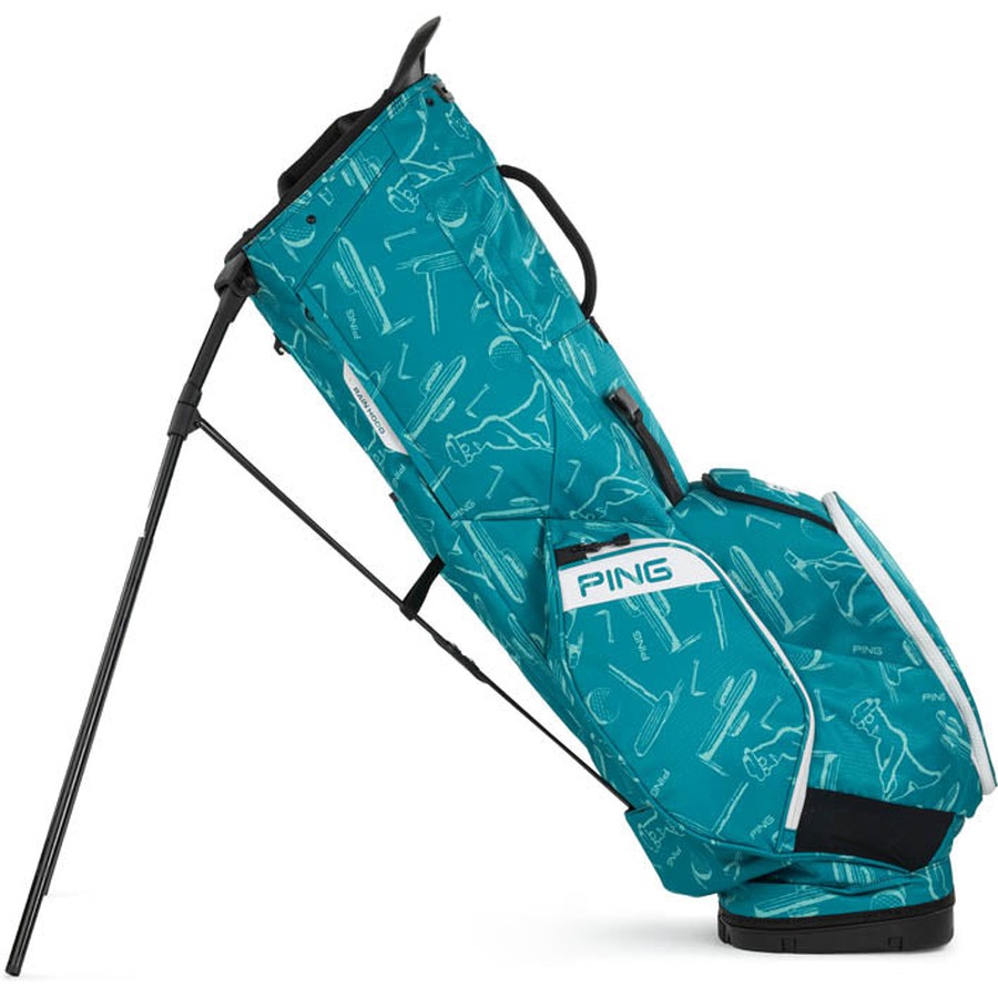 The Ping Hoofer 231 Golf Carry Bag features a teal design with white abstract golf-themed graphics, black stand legs, a white Ping logo, and offers up to 16 zippered pockets for organized storage.
