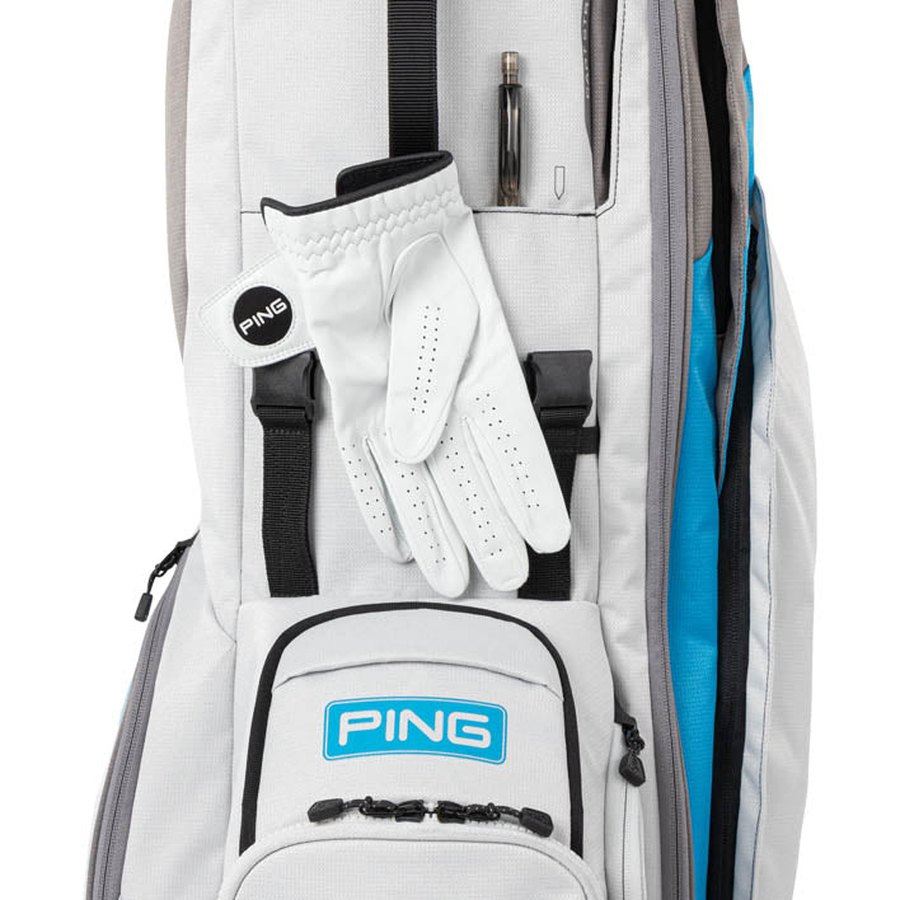 A close-up shows the lightweight Ping Hoofer 231 Golf Carry Bag with a white golf glove on the front, a black and white ball marker, a zippered pocket featuring the PING logo, and a pen in a vertical slot near the top.