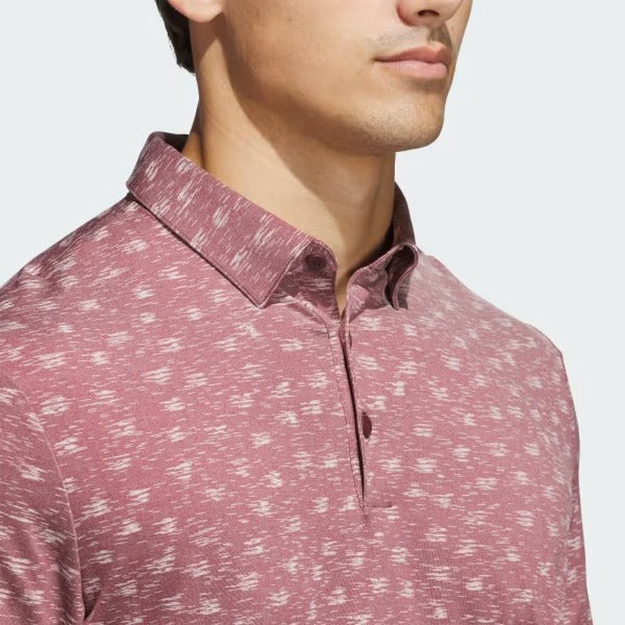 A man is shown from the shoulders up against a plain background, wearing the adidas Ultimate365 Novelty Polo Shirt in burgundy, which features a collar and is made from recycled materials.
