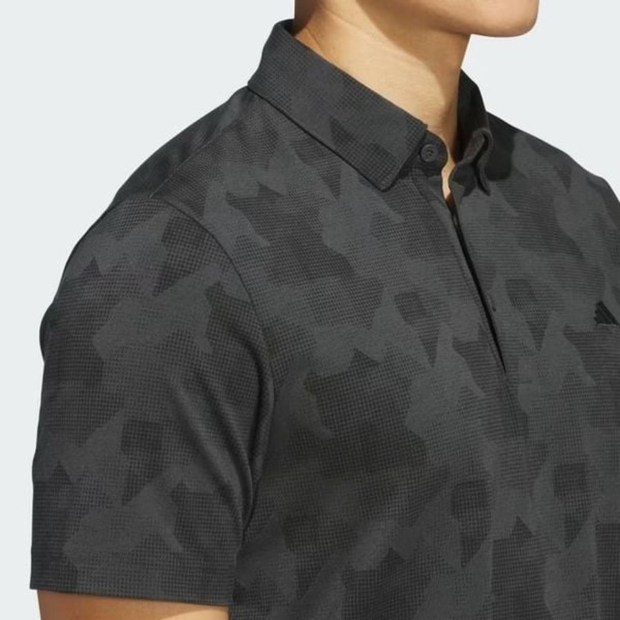 A person wears the Adidas 2025 Go-To Printed Polo Shirt in dark gray with a subtle geometric pattern, made from recycled materials, shown from shoulders to mid-chest against a light background.