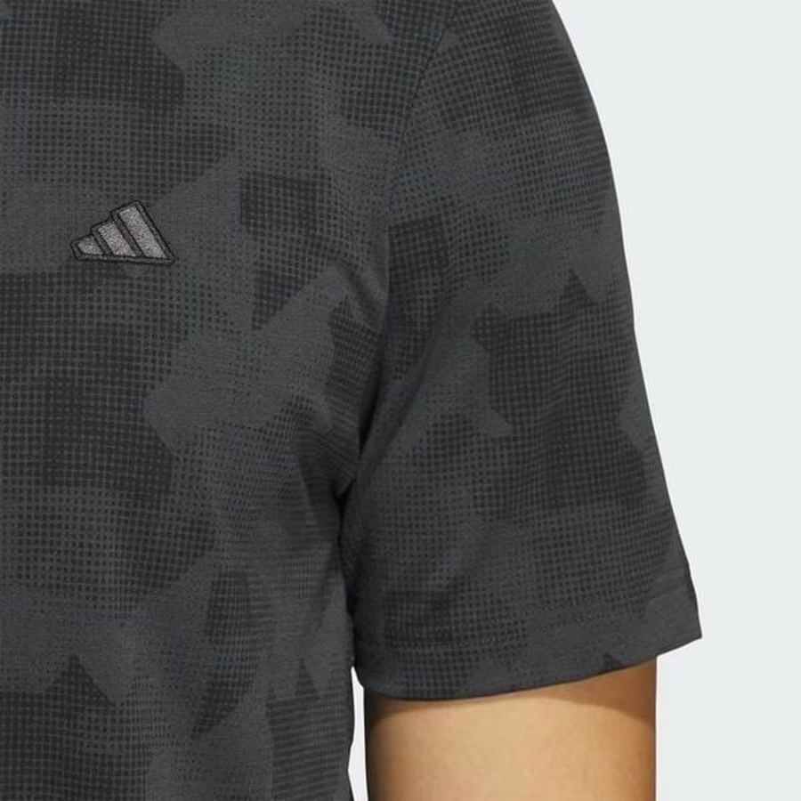 Close-up of a person wearing the Adidas 2025 Go-To Printed Polo Shirt, featuring a black patterned design. Only the upper torso and right arm are visible against a light gray background.