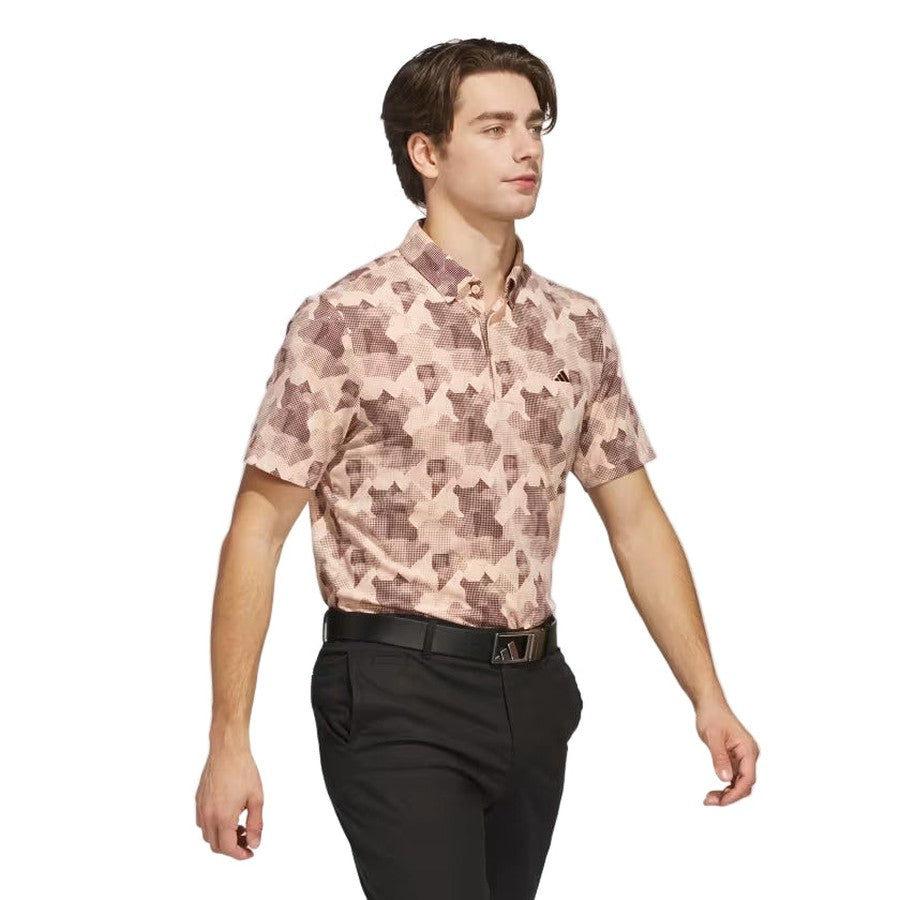 A man confidently walks against a plain white background wearing the Adidas 2025 Go-To Printed Polo Shirt, a short-sleeve pink and brown golf polo made with recycled materials.