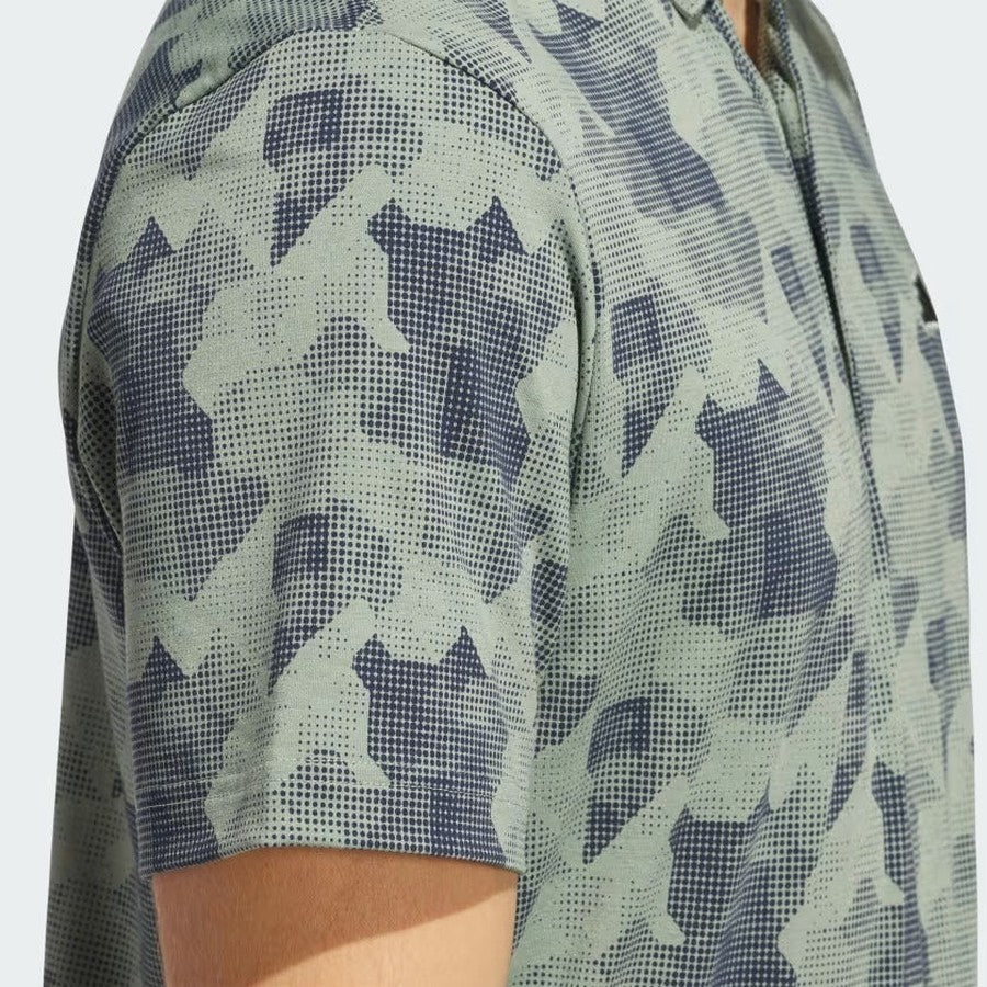 Close-up of a person wearing the Adidas 2025 Go-To Printed Polo Shirt in green and navy, featuring geometric and dotted patterns. Only the upper torso and arm are visible; this men’s golf polo is made with recycled materials.