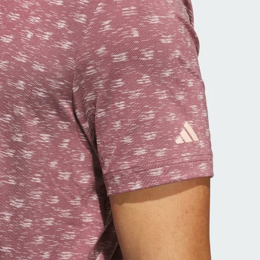 Close-up of a person’s upper arm wearing an Adidas Ultimate365 Novelty Polo Shirt in burgundy, made with recycled materials. The adidas logo appears near the sleeve hem.