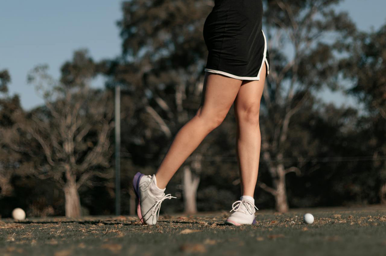 detail of a woman golf player shoes while she swings a club in the golf field