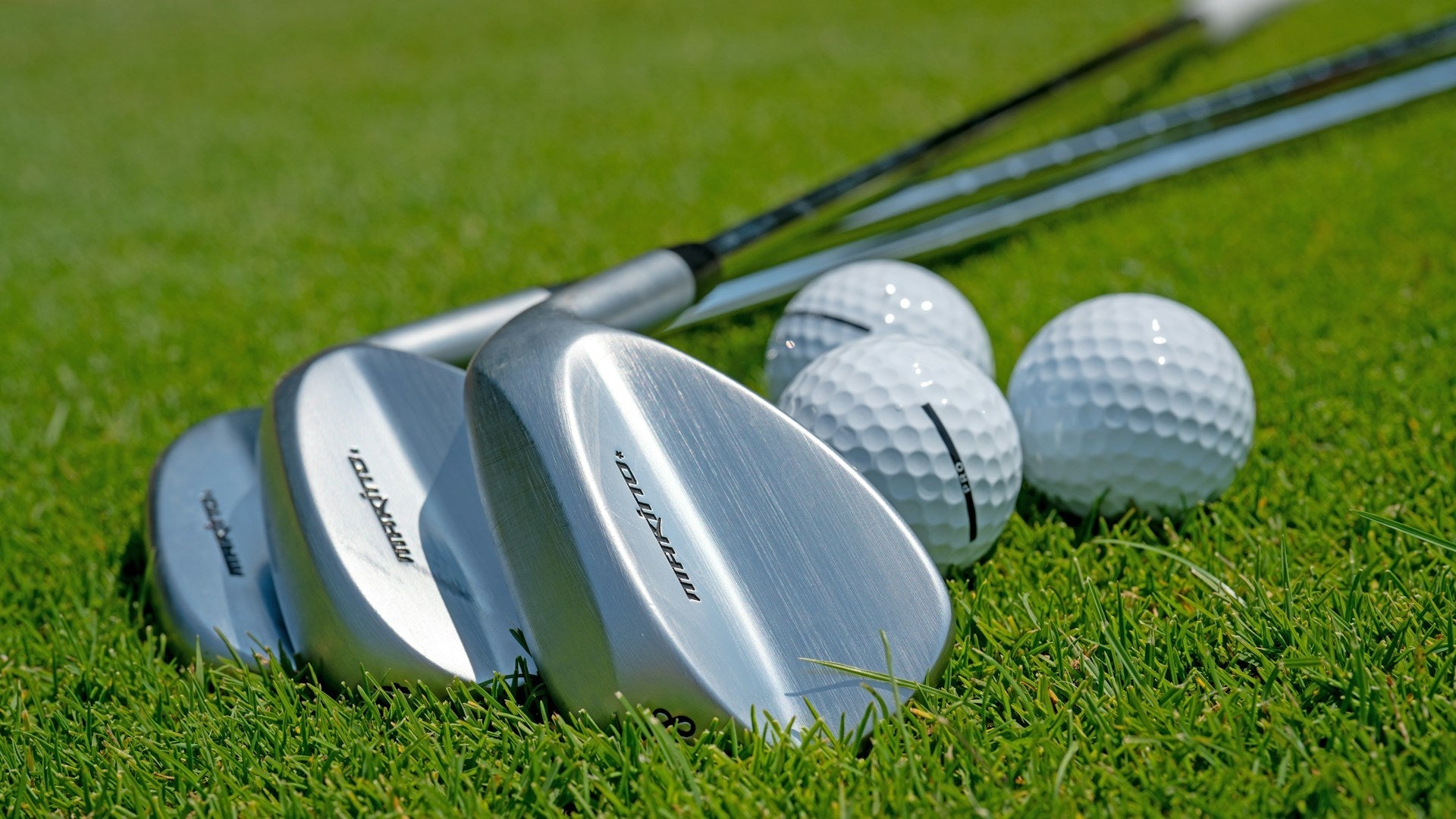 golf wedges laid out in a green grass with golf balls by them
