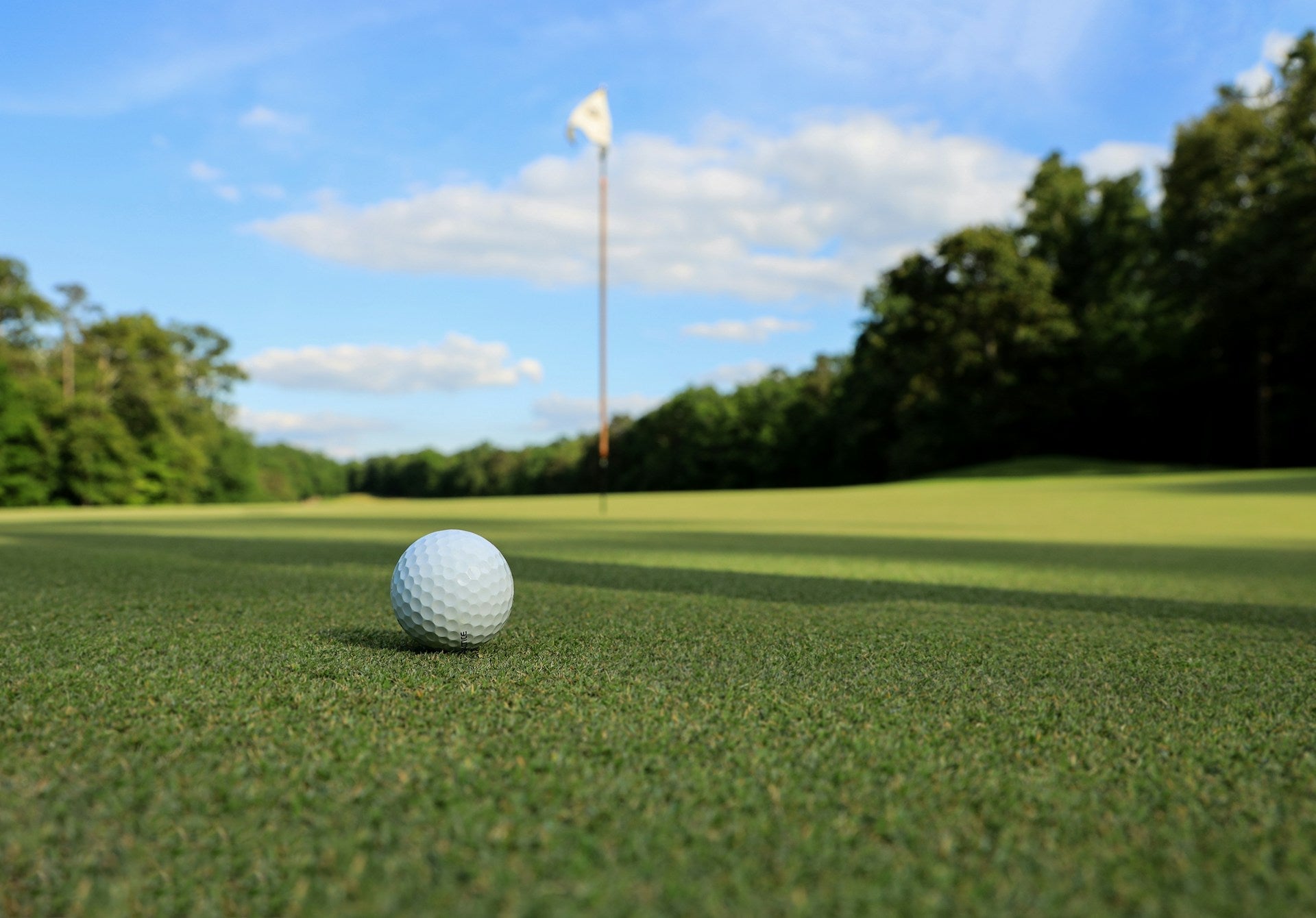 golf ball in the middle of a green golf field with a flag pole in the background