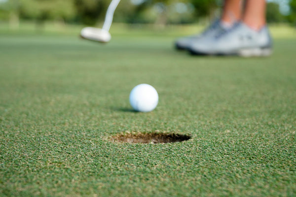 light putter or heavy putter white golf ball next to golf hole after hit by player