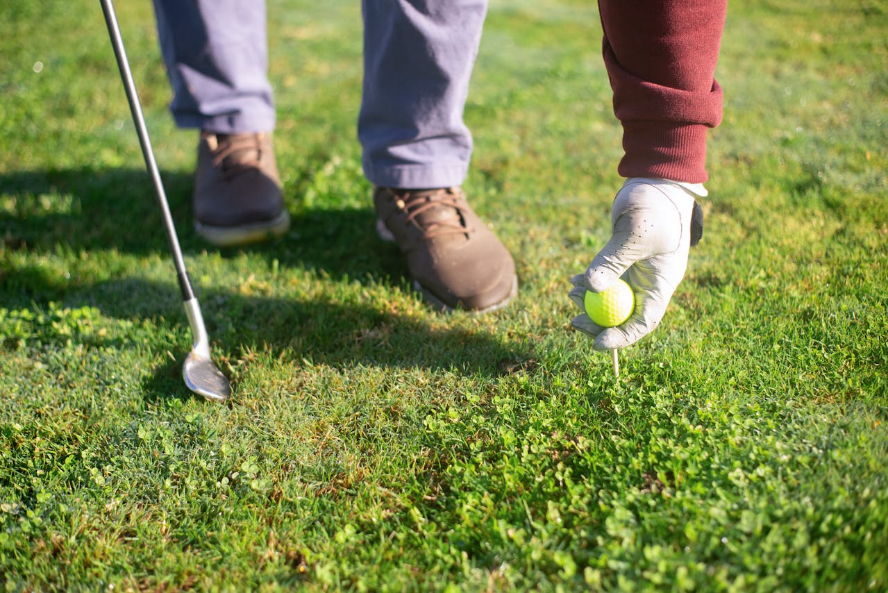 pro golf player adjusting ball on tee detail of the shoes he's wearing