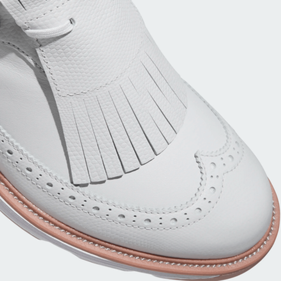 Close-up of the Adidas MC Zoysia Ladies Spikeless Golf Shoes in grey, featuring a white leather upper, tan sole, and decorative fringe on top—blending classic brogue style with modern comfort for women golfers.