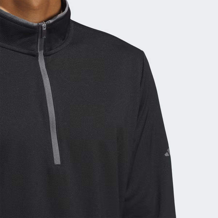 A person wears the Adidas Lightweight Half-Zip Top in black, featuring a gray zipper and small left-sleeve logo. Shown from shoulders to chest. Made with recycled materials for eco-friendly appeal. Final sale item.
